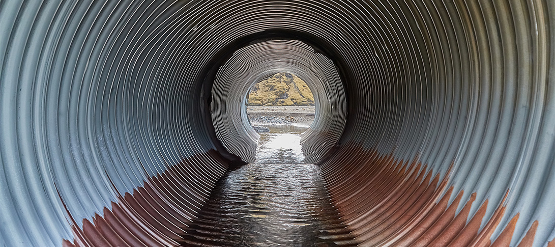 photo: inside a large culvert pipe with water flowing along the bottom