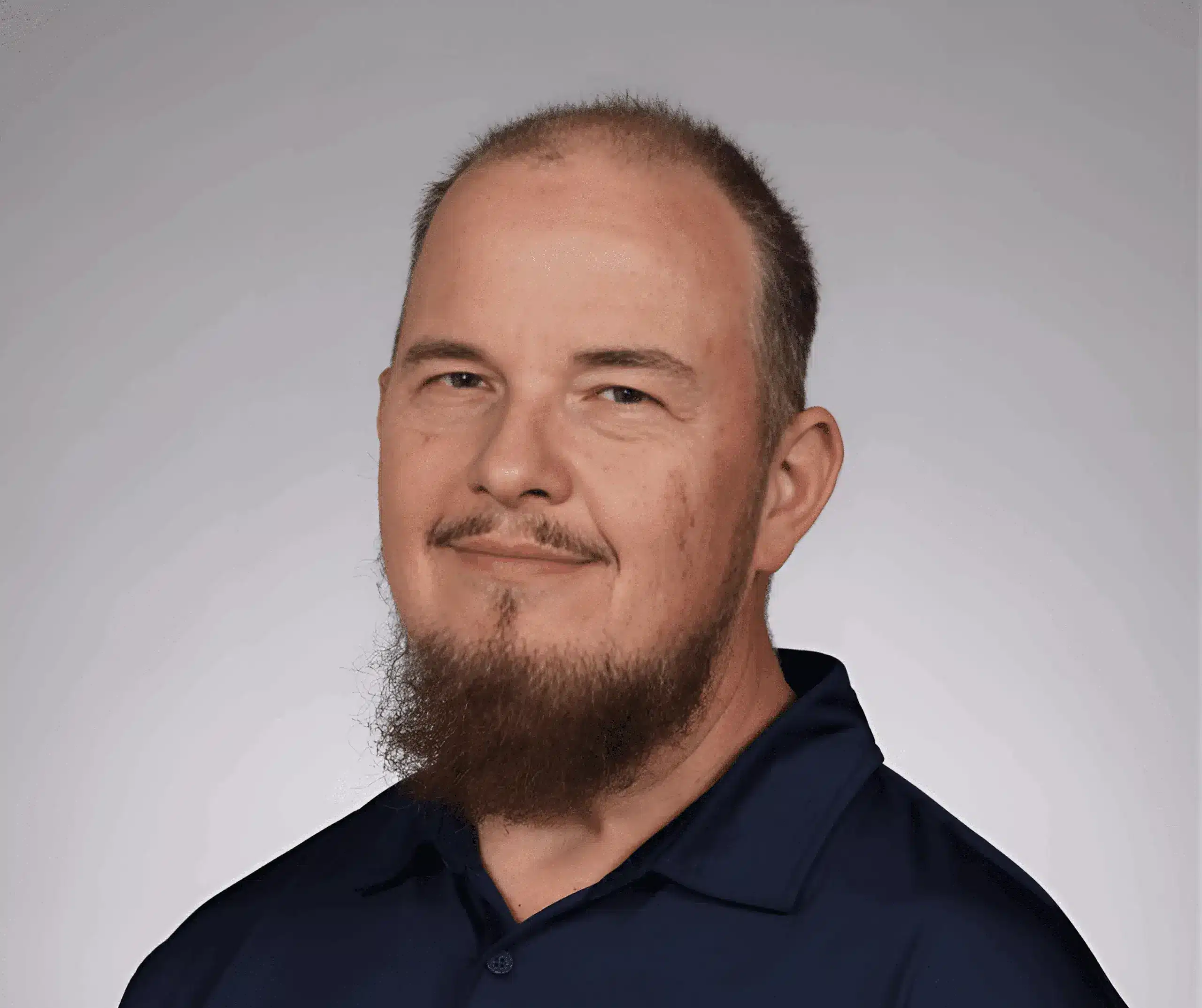 A middle-aged man with a trimmed beard and short hair, dressed in a dark collared shirt, poses confidently in front of a plain gray background, embodying the professionalism of pond management.