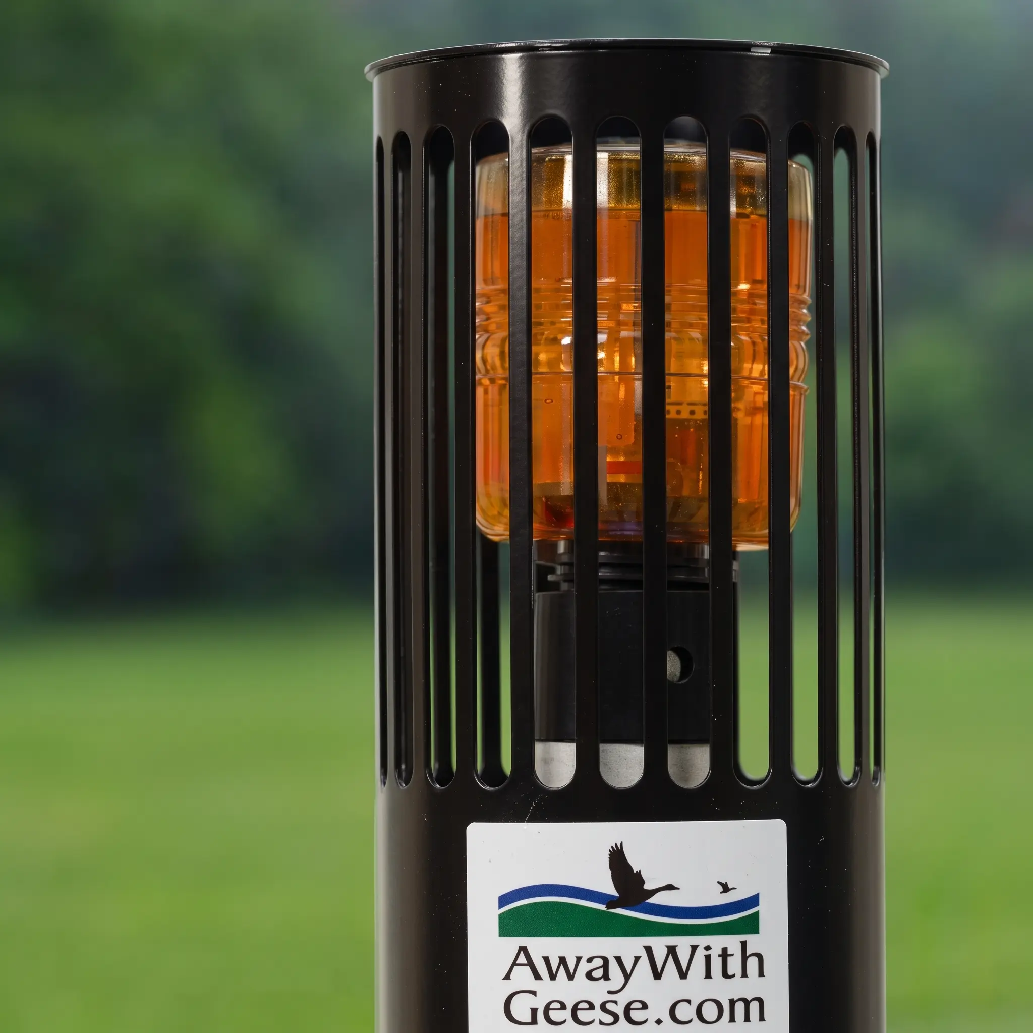 Close-up of a black cylindrical device with an amber light inside, labeled “AwayWithGeese.com,” set against a blurred grassy background.